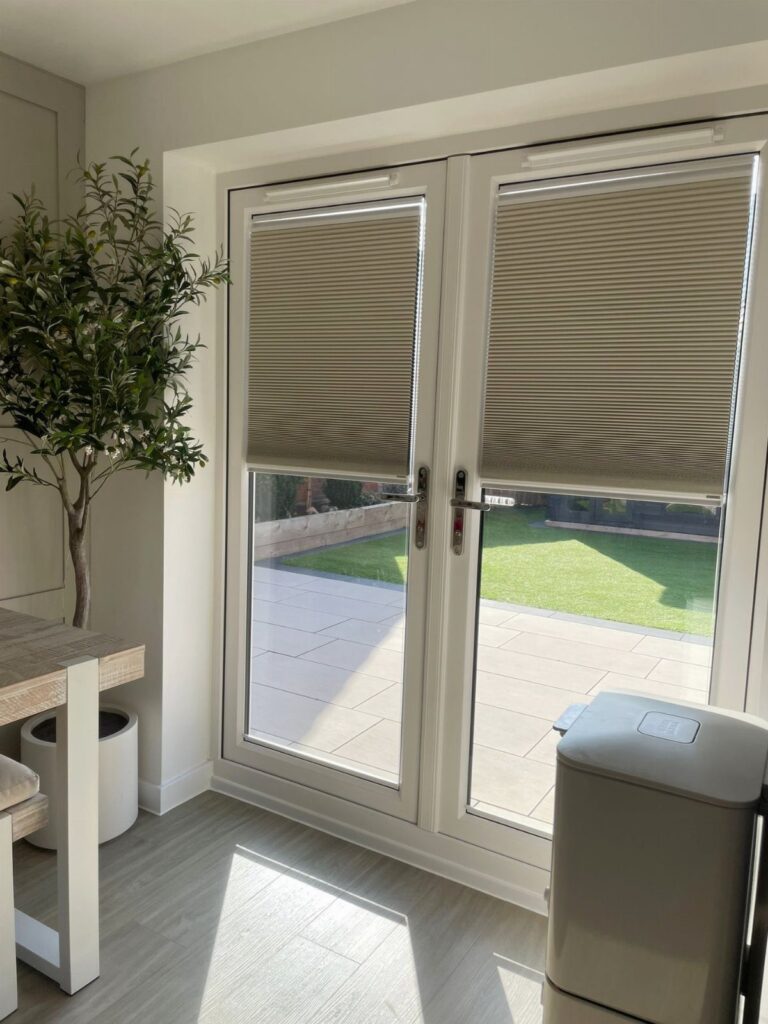 Beige cellular shades covering the upper half of white French doors leading to a garden.