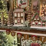 Decorated gingerbread houses and miniature trees arranged on a festive mantelpiece with greenery.