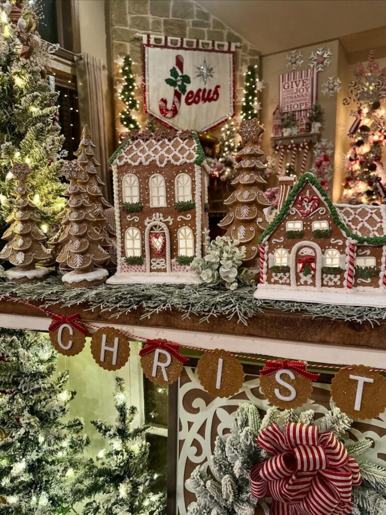 Decorated gingerbread houses and miniature trees arranged on a festive mantelpiece with greenery.