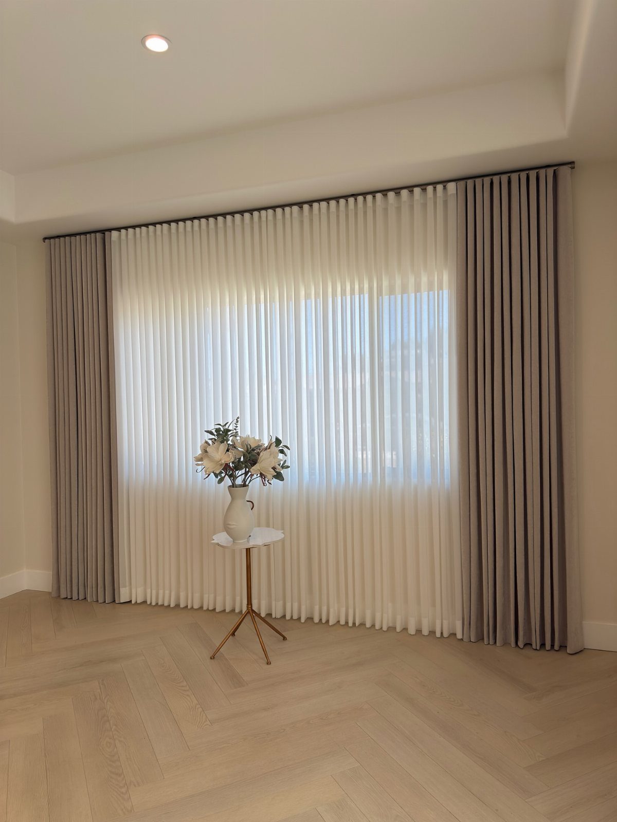 Beige and white pleated curtains hanging over a large window in a bright room.