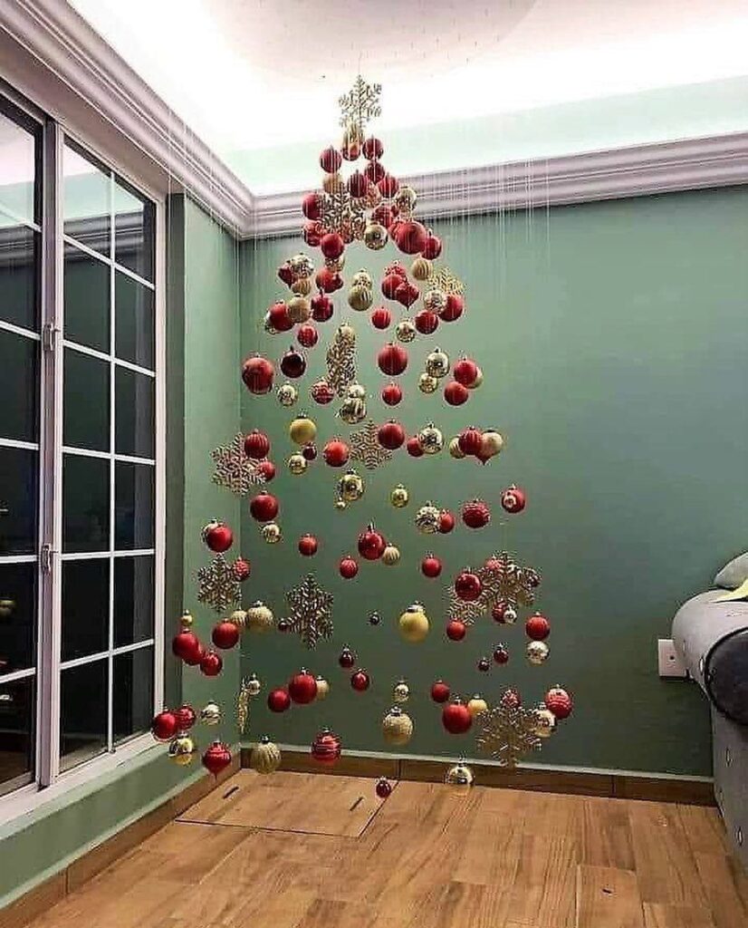 Red and gold ornaments hanging from the ceiling to form a Christmas tree shape against a green wall.