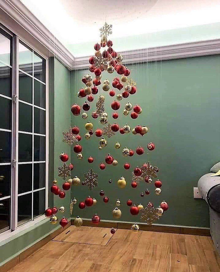 Red and gold ornaments hanging from the ceiling to form a Christmas tree shape against a green wall.