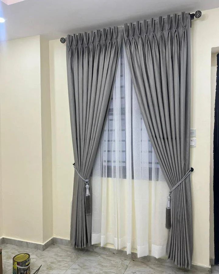 Two grey curtain panels tied back with cords over white sheer curtains on a window.