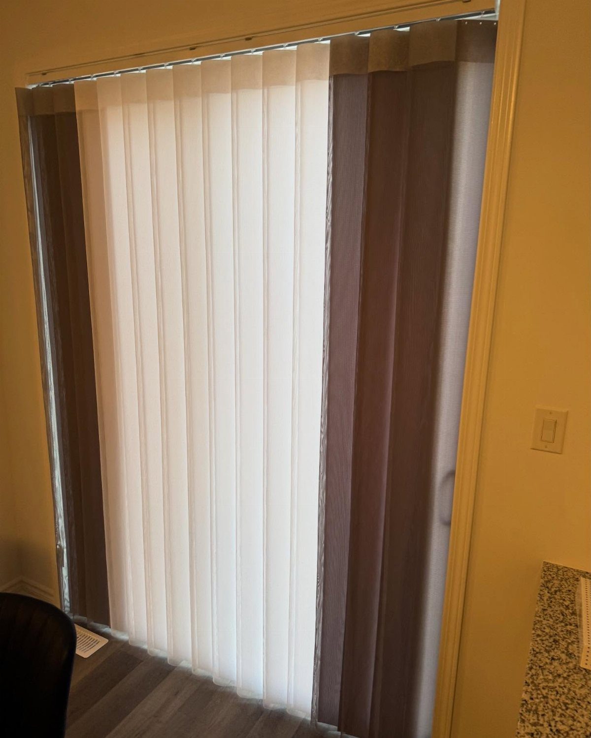 Vertical blinds in alternating white and dark brown colors hanging over a sliding glass door.