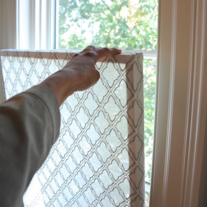 A person holding a patterned DIY privacy window screen frame up to a bright window.
