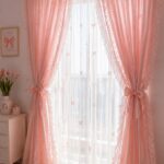 Pink ruffled sheer curtains with bow details hanging over a bright window in a bedroom.