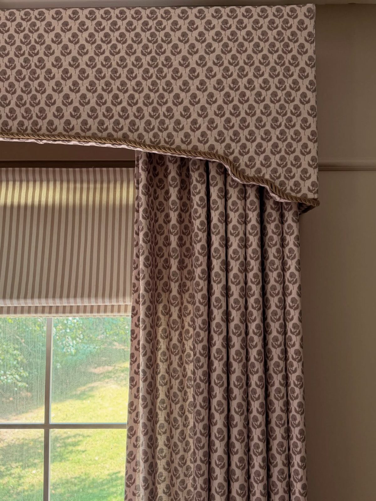 Patterned fabric upholstered cornice with a scalloped edge hanging above matching curtains and a striped shade.