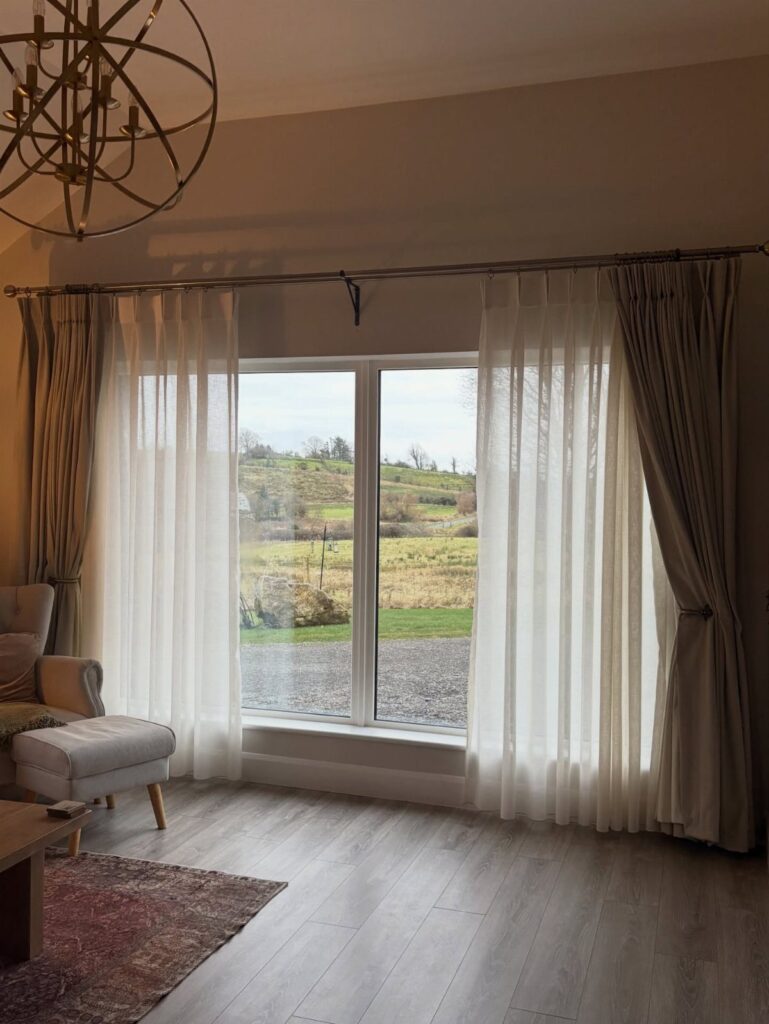 Sheer white curtains and beige drapes hanging over a large window in a living room.