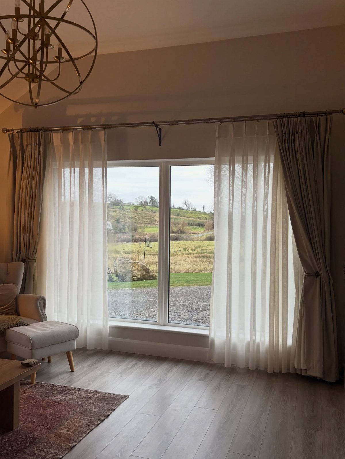 Sheer white curtains and beige drapes hanging over a large window in a living room.