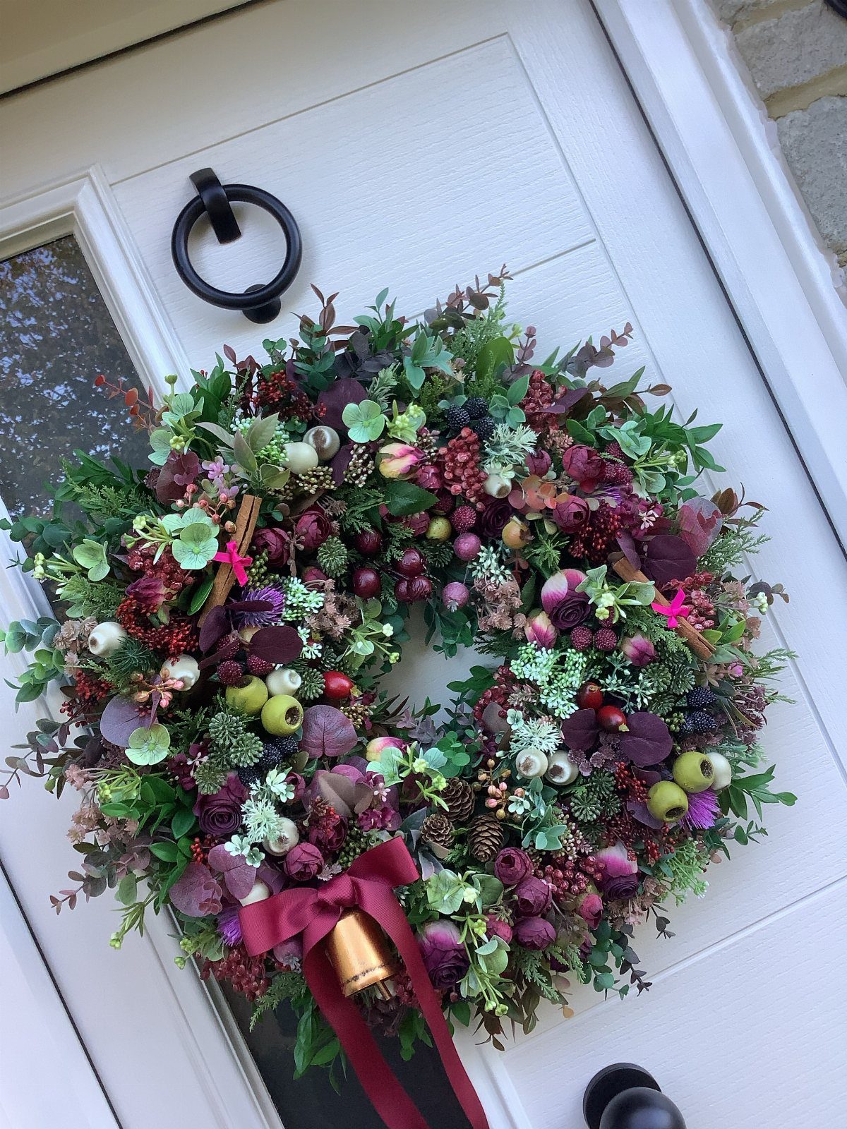 A lush Christmas wreath with red berries and a gold bell hanging on a white door.
